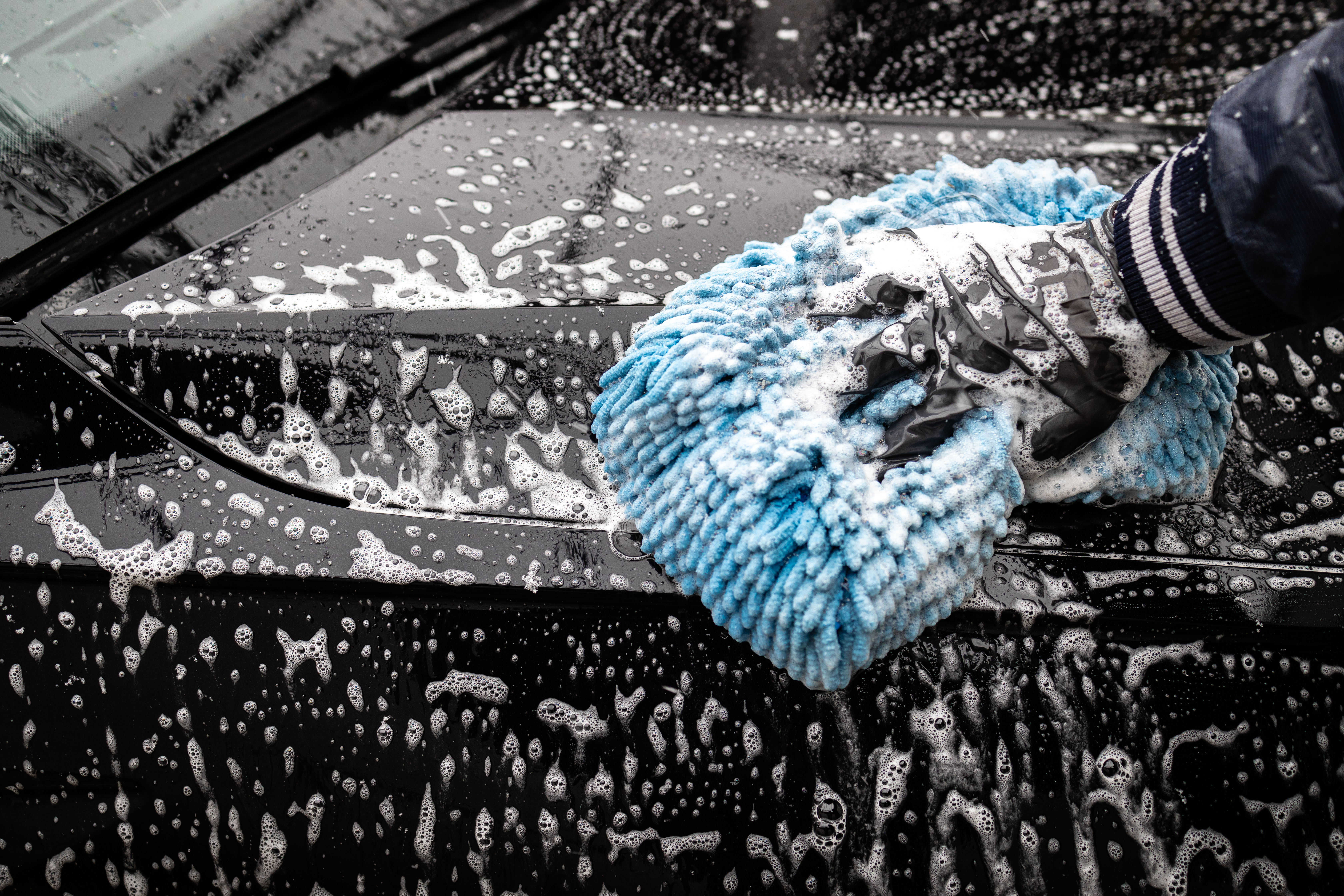 foam-automotive-detailer-washing-black-car-indoors-vehicle-cleaning-facility-bright-day